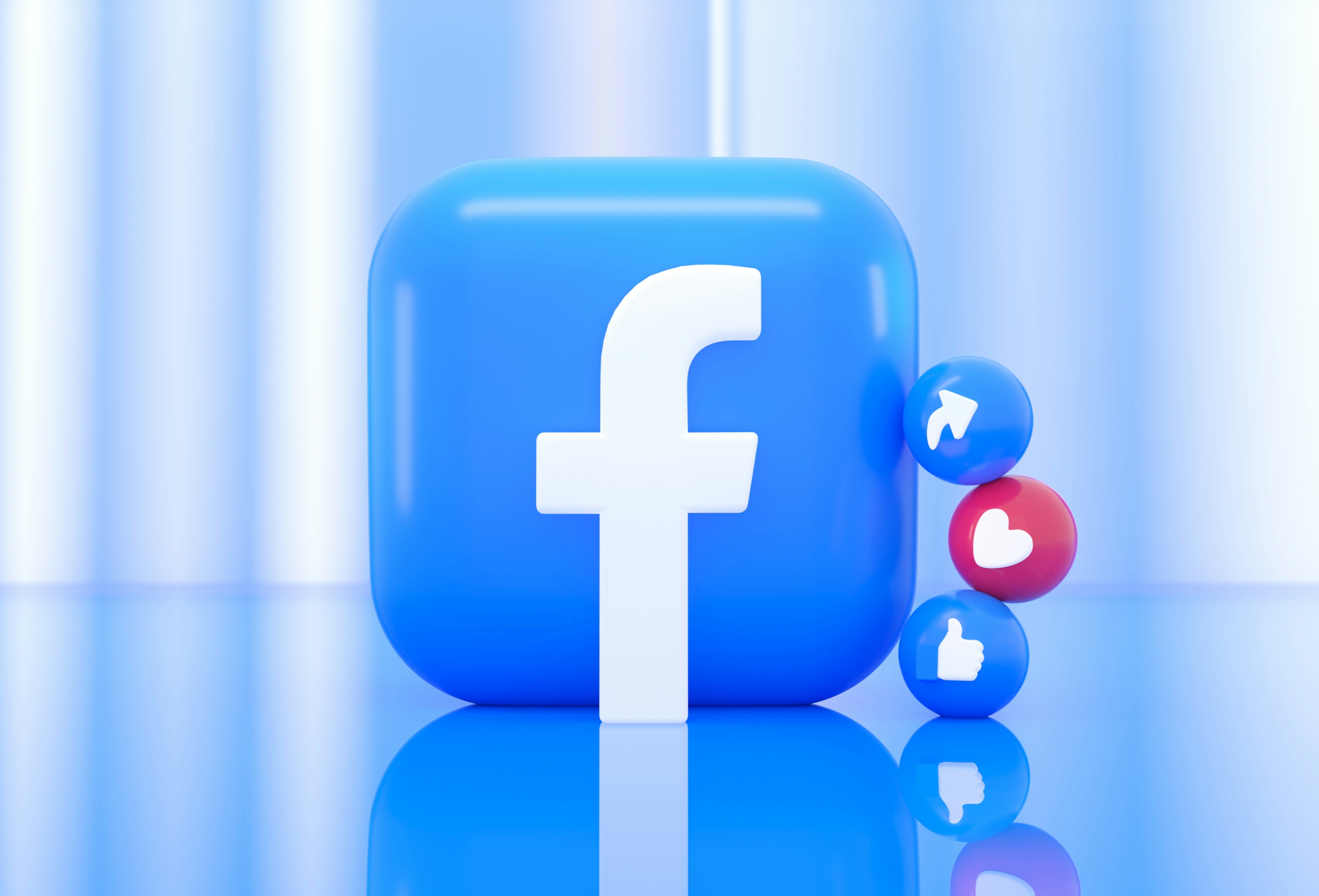A blue, glossy Facebook icon is centered with smaller emoji spheres for like, love, and vote reactions stacked beside it, set against a blurred blue background.